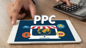 Tablet displaying PPC concept with icons for online shopping, video, podcast, and ads; a hand points to the screen, and a calculator is visible nearby.