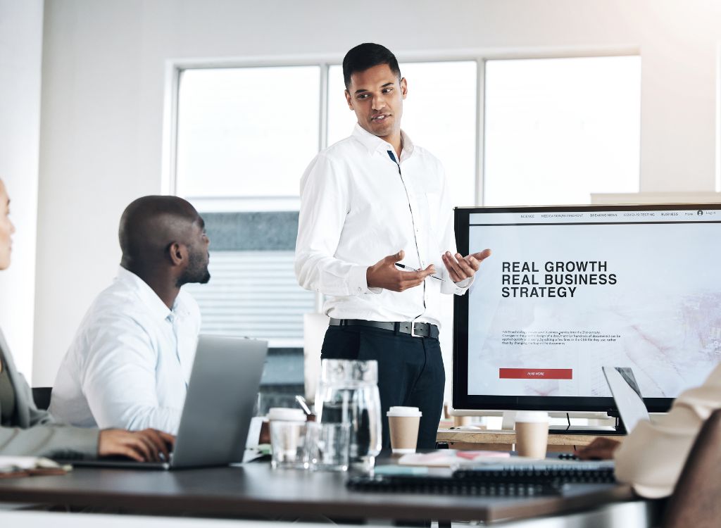 An image showing two individuals and a laptop. The person standing is talking about SEO strategy.